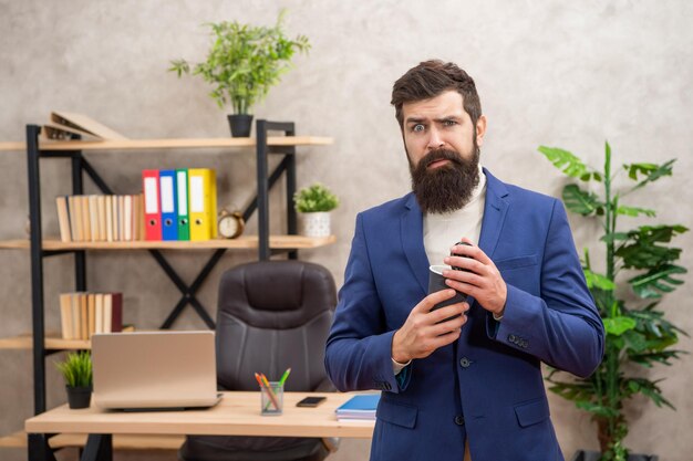 Обеспокоенный бизнесмен держит пустую одноразовую чашку кофе во время офисного перерыва на вынос