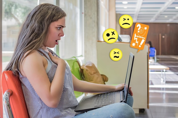 Photo anxious caucasian female using her laptop with different emoticons around