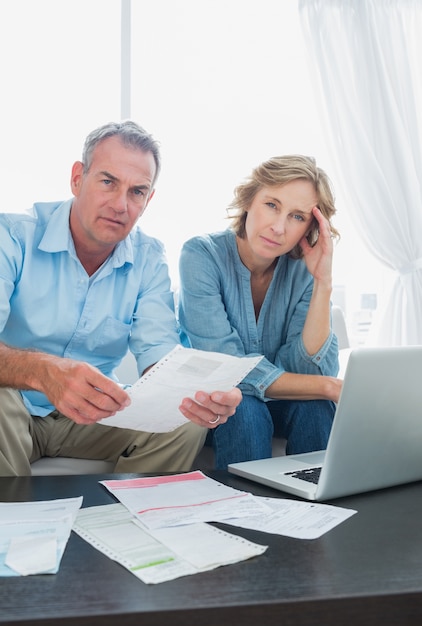 Anxious couple paying their bills online with laptop looking at camera