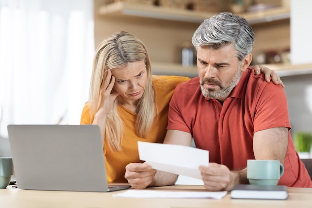 Anxious middle aged husband and wife checking correspondence kitchen interior