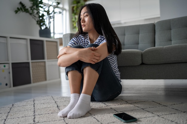 Anxious sad depressed asian woman sits alone on floor lost hope thinks about problem feels abandoned