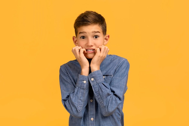 Foto ragazzo adolescente ansioso in camicia denim che si morde le unghie e guarda la telecamera