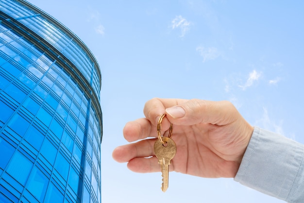 Apartment key in a man's hand. Brass house door lock key. Modern building, view from below. Architecture in modern city. Sale and rental of real estate.