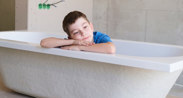Apartment renovation. Creative story young happy boy sits in a bathtub in the middle of the room. Empty walls, DIY home renovation.