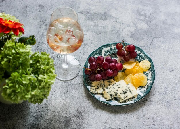 Aperitiefcocktail en een bord met druivenkaas en chips op een grijze bovenaanzicht als achtergrond