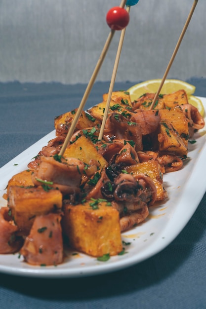 Aperitif or typical Spanish tapa baby squid with garlic and potatoes served on an elongated white