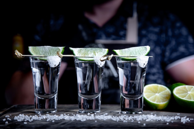 Aperitif with friends in the bar, three glasses of alcohol with lime and salt for decoration. Tequila shots, selective focus