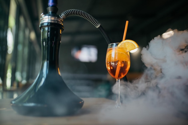 Aperolspritzカクテルレストランの背景にある水ギセルHookahの近くのAperolspritzフッカースモークテーブルの上のおいしい水ギセルスプリッツ