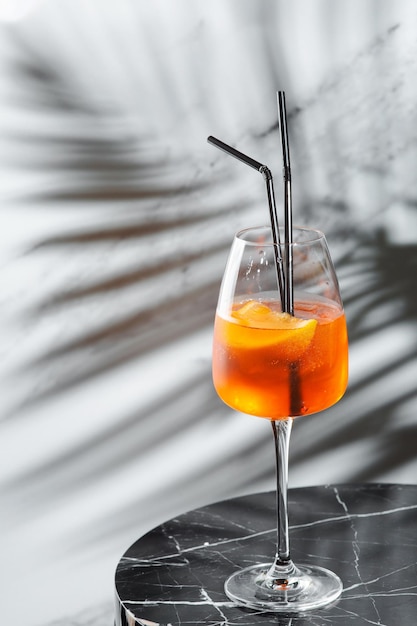 Aperol Spritz cocktail in glass and sliced orange on marble table. summer mood concept. cocktail with ingredients and shadow of branch on light background.