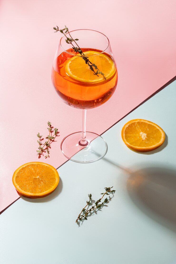 коктейль Aperol Spritz на розовом и синем фоне с апельсинами и розмарином