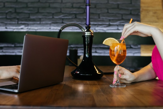 Aperol spritz in de handen van een meisje Aperol spritz Cocktail Waterpijp en aperol op de tafel bij de laptop De samenstelling van het restaurant met waterpijp en aperol