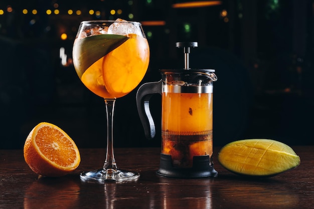 Aperol spritz and mango tea in french press on dark wooden background