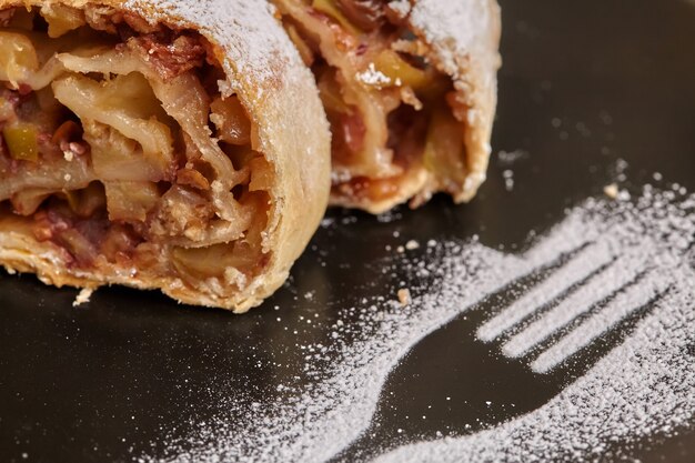 Apfelstrudel met poedersuiker op zwarte plaat, houten muur