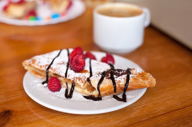 Apfelstrudel met poedersuiker, verse frambozen en chocoladeroom. een kopje zwarte koffie