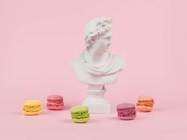 Статуя Аполлона и миндальное печенье разбросаны на розовом фоне Минимальная концепция