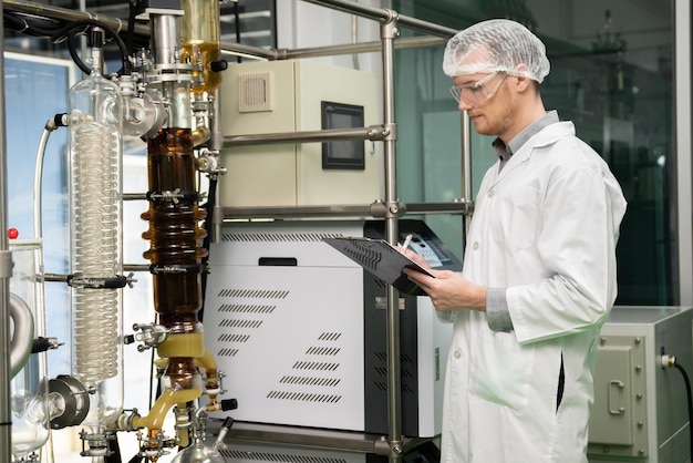 Apothecary scientist recording data from CBD oil extractor in laboratory