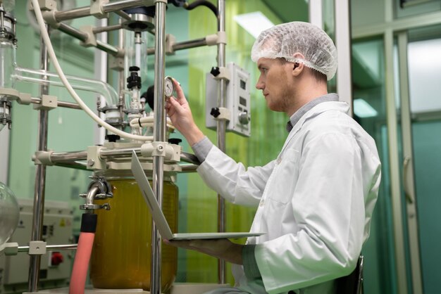 Photo apothecary scientist recording data from cbd oil extractor in laboratory