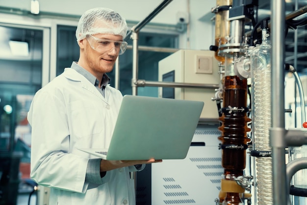 Ученый-аптекарь, работающий с ноутбуком возле экстрактора масла CBD в лаборатории