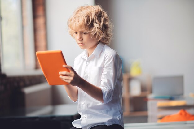 App. ragazzo biondo sveglio che tiene il suo tablet e digitando un messaggio