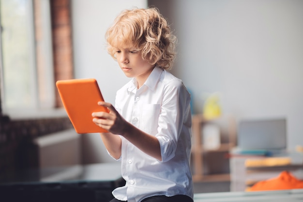 App. Schattige blonde jongen houdt zijn tablet en een bericht typen