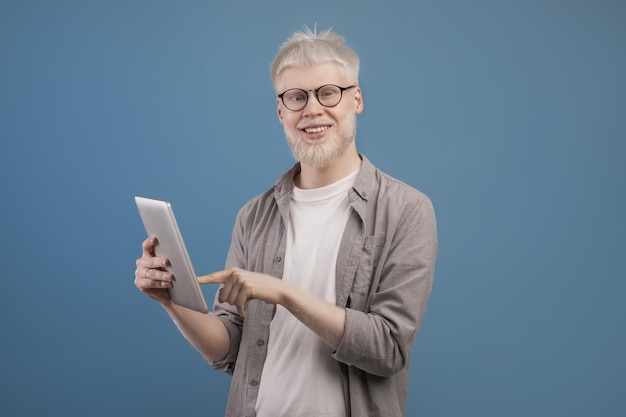 Apparaat voor werk entertainment en communicatie gelukkige albino man met behulp van digitale tablet op blauw