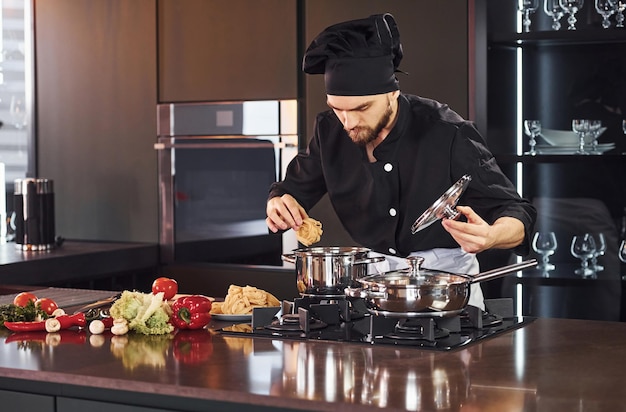 Apparatuur gebruiken Professionele jonge chef-kok in uniform die met groenten aan de keuken werkt