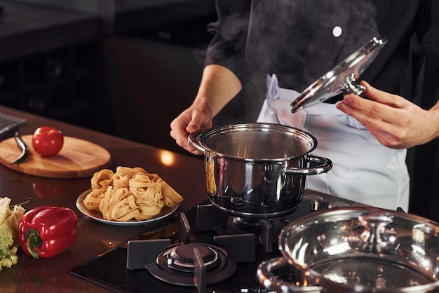 Apparatuur gebruiken Professionele jonge chef-kok in uniform die met groenten aan de keuken werkt