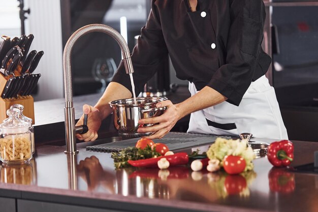 Apparatuur gebruiken Professionele jonge chef-kok in uniform die met groenten aan de keuken werkt