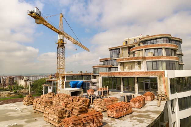 Appartement of kantoor hoog gebouw in aanbouw. Bakstenen muren, glazen ramen, steigers en betonnen steunpilaren. Torenkraan op de heldere blauwe ruimteachtergrond van het hemelexemplaar.