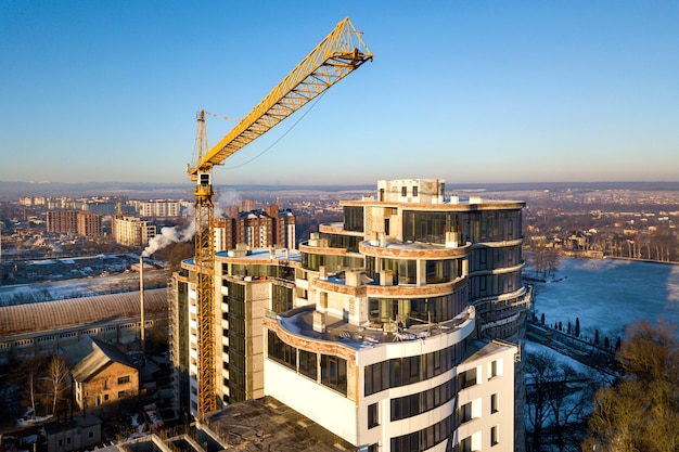 Appartement of kantoor hoog gebouw in aanbouw, bovenaanzicht. Torenkraan op de heldere blauwe ruimte van het hemelexemplaar, stadslandschap het uitrekken zich aan horizon. Drone luchtfotografie.