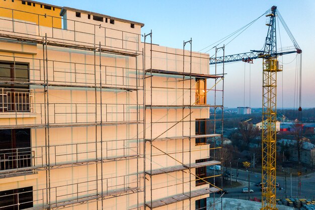 Appartement of kantoor hoog onvoltooid gebouw in aanbouw. Bakstenen muur in steigers, glanzende ramen en torenkraan op stedelijk landschap en blauwe hemel. Drone luchtfotografie.