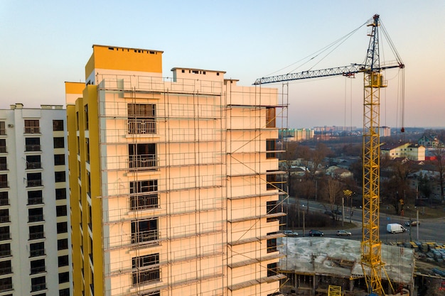 Appartement of kantoor hoog onvoltooid gebouw in aanbouw. Bakstenen muur in steigers, glanzende ramen en torenkraan op stedelijk landschap en blauwe hemel. Drone luchtfotografie.