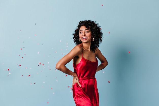 Appealing mixed race girl standing under confetti Studio shot of laughing curly woman in red dress