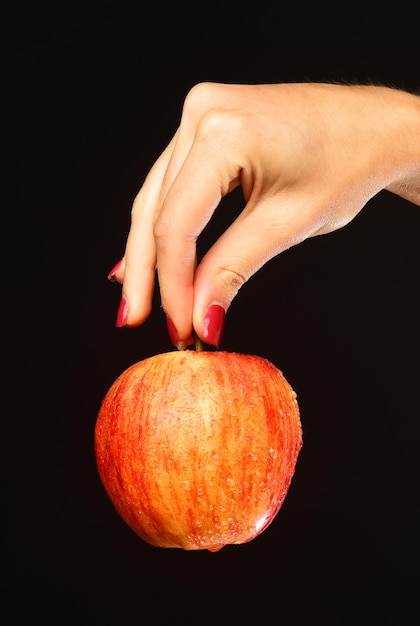 Appel in rode en oranje kleur in meisjesvingers. landbouw en gezond voedingsconcept. herfst tuinieren idee. vrouwelijke hand houdt vers fruit geïsoleerd op zwarte achtergrond.