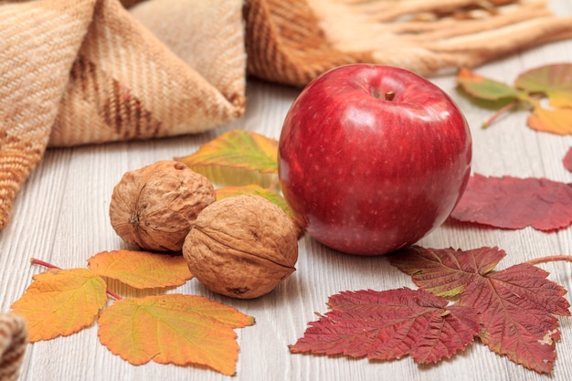 Appel, walnoten, geruite plaid en droge bladeren op houten planken. Een herfstcompositie.