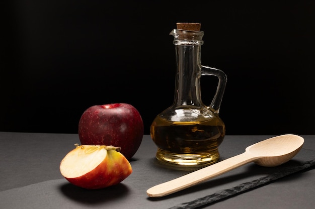 Appelazijn in de glazen fles met een kurk, een houten lepel, een verse rode appel en een gesneden