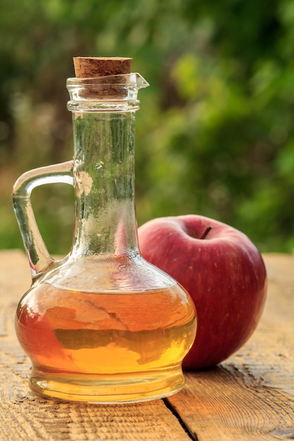 Appelazijn in glazen fles met kurk en verse rode appel op oude rustieke houten planken.