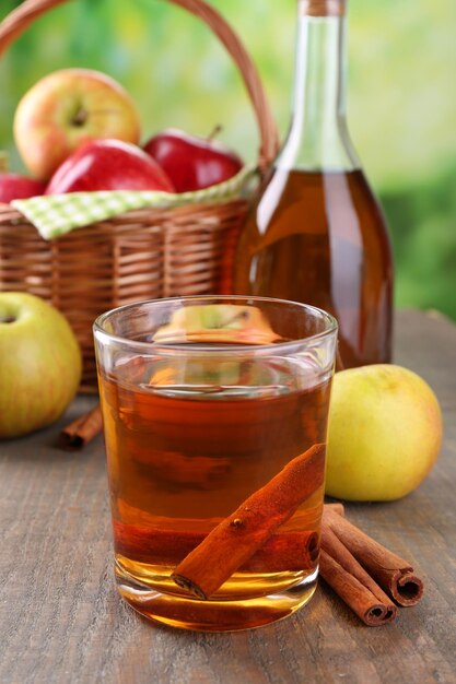 Appelcider in glas en fles met kaneelstokjes en verse appels op houten tafel op lichte achtergrond