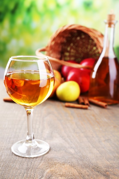 Appelcider in wijnglas en fles, met kaneelstokjes en verse appels op houten tafel, op lichte muur