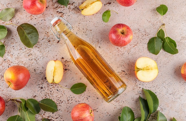 Appelciderazijn in een glazen fles en verse appels met bladeren op beige betonnen achtergrond bovenaanzicht close-up