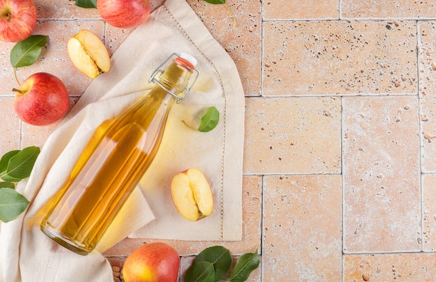 Appelciderazijn in een glazen fles en verse appels met bladeren op beige betonnen ondergrond bovenaanzicht plat lag