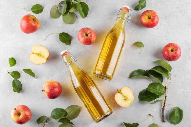 Appelciderazijn in twee glazen flessen en verse appels met bladeren op lichte achtergrond bovenaanzicht plat lag