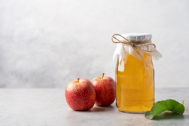 Appelciderfles en rode appels op lichtgrijze achtergrond