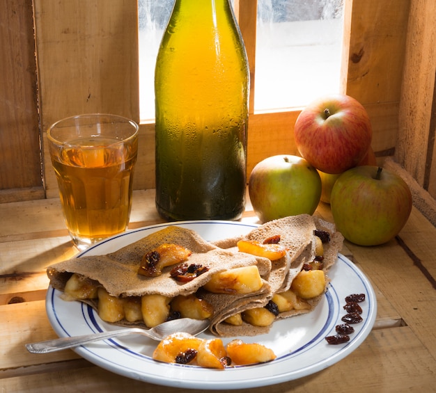 Appelpannenkoekjes met een fles en een glas cider naast een raam