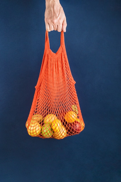 Appels en citroenen in een oranje koordzak in de hand van een man