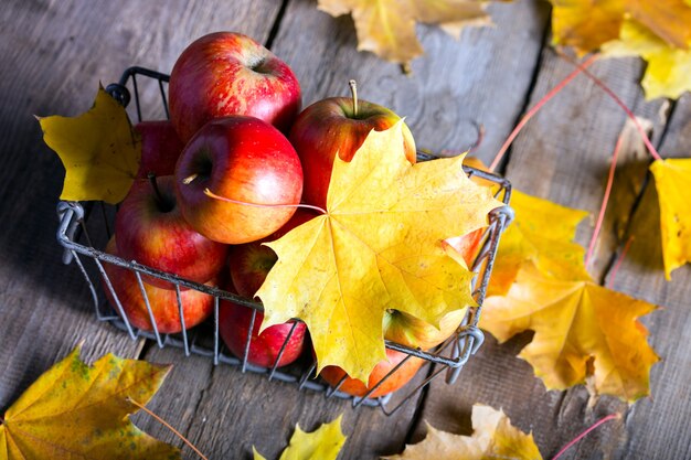 Appels in een mand op een houten tafel en gele esdoornbladeren