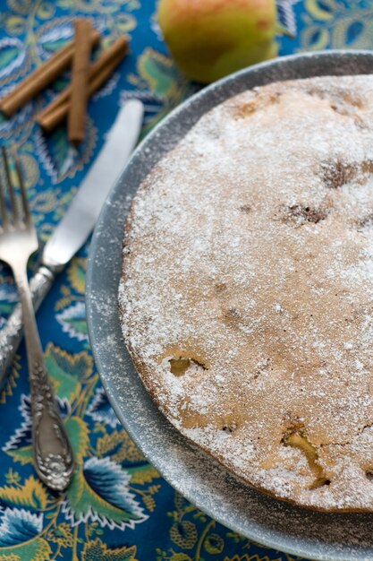 Appeltaart is de grijze plaat, liggend naast vork, mes, kaneelstokjes en appels op fel