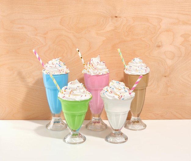 Appetiserende zoete kleurrijke milkshakes met zachte witte room en gekleurde besprenkels in glazen op een houten achtergrond Feestelijke en kleurrijke stemming