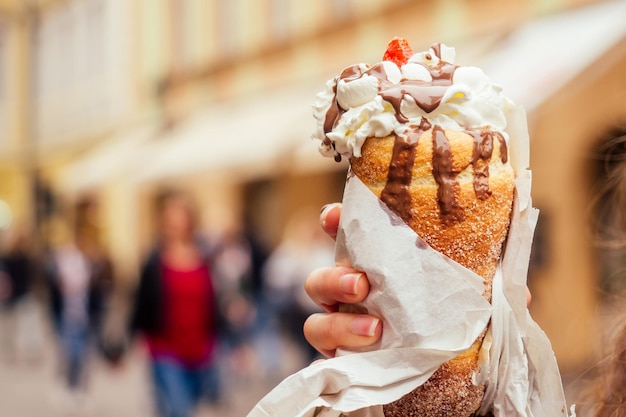 Appetite eats a traditional Czech sweet Trdelnik with vanilla cream and strawberries in Prague street