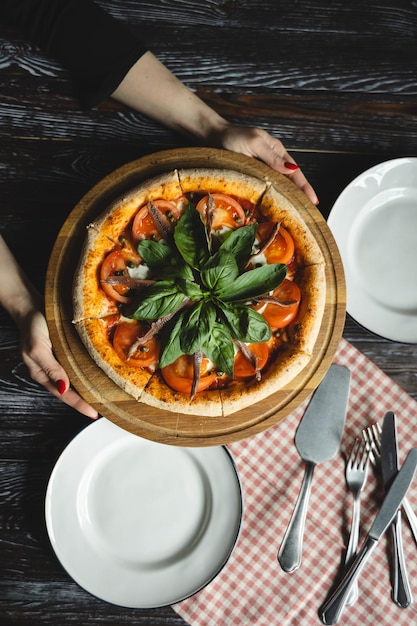 Foto appetitieve pizza met tomaten, ansjovis en basilicum op een houten achtergrond